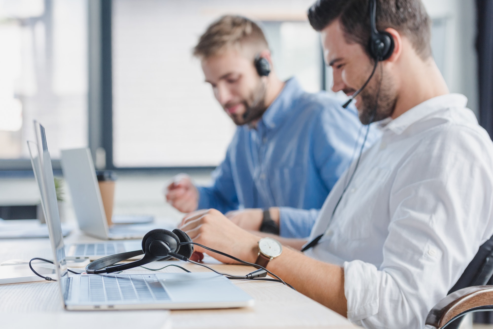 smiling-young-call-center-operators-in-headsets-using-laptops-in-office.jpg